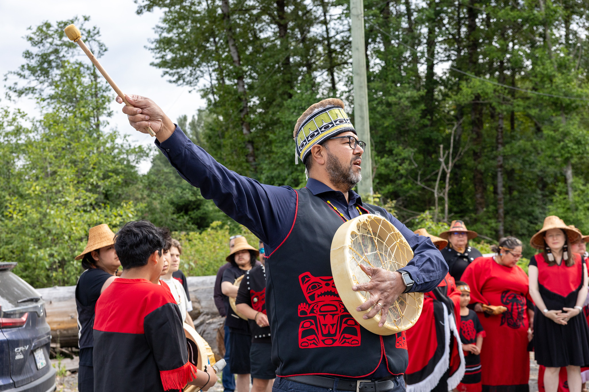 Man with drum standing in a group of people wearing ceremonial clothing